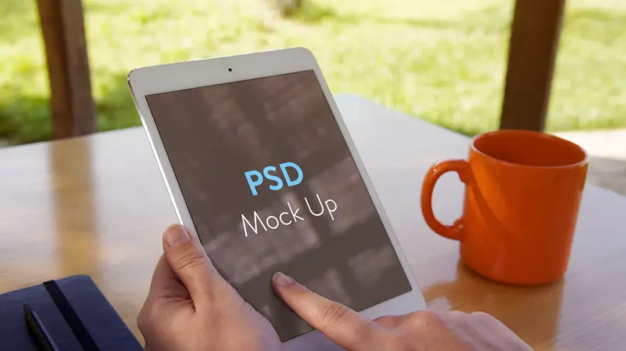 Download Tablet in hand and a cup on the table PSD mockup